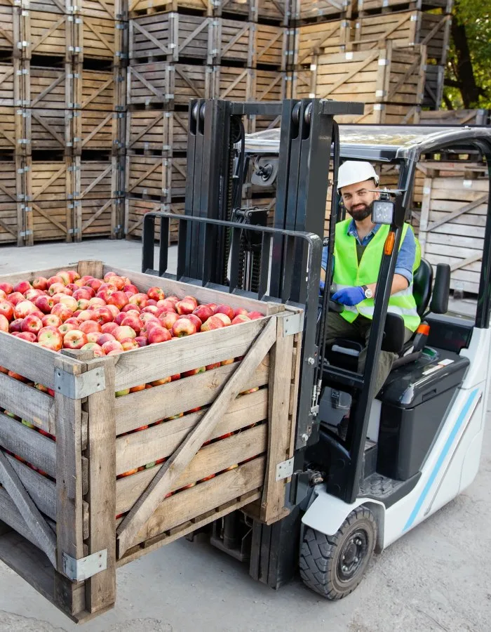 Forklift operator in a hard hat moving a bin of apples